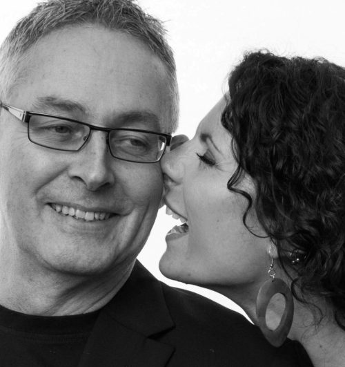 Elinor Hamilton whispering in Phil Sayer's ear. Both are smiling.